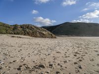 the sandy beach in front of the hills is empty and very wide with some footprints left in the sand