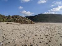 the sandy beach in front of the hills is empty and very wide with some footprints left in the sand