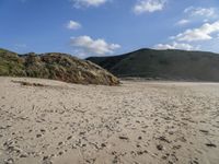 the sandy beach in front of the hills is empty and very wide with some footprints left in the sand