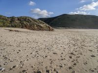 the sandy beach in front of the hills is empty and very wide with some footprints left in the sand