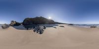 sand on the beach and large rock formation near the ocean with the sun rising behind