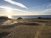 this is a sunset over the ocean near some rocks and sand area at the shoreline