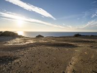 this is a sunset over the ocean near some rocks and sand area at the shoreline