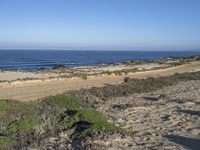 people walking along the road on the beach near the ocean waves and sand hills and scrubland