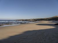 a man and woman walking down the beach near the ocean shore to a small cove