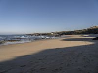 a man and woman walking down the beach near the ocean shore to a small cove