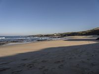 a man and woman walking down the beach near the ocean shore to a small cove