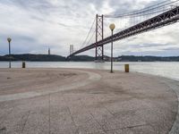 an empty beach with benches under an overpass bridge in the background and water in the foreground