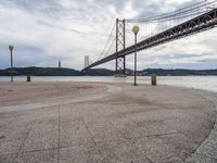 an empty beach with benches under an overpass bridge in the background and water in the foreground