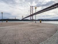 an empty beach with benches under an overpass bridge in the background and water in the foreground