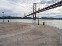 an empty beach with benches under an overpass bridge in the background and water in the foreground