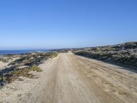 a dirt road on the sea shore with a blue sky background and clear water to the left