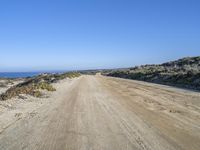 a dirt road on the sea shore with a blue sky background and clear water to the left