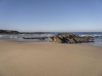 sand beach with rocks and waves crashing in the background at low tide by sea shore