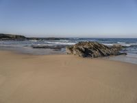 sand beach with rocks and waves crashing in the background at low tide by sea shore