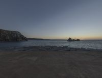 sunset view of rock formations with beach and ocean in background at dusk with blue sky