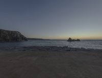 sunset view of rock formations with beach and ocean in background at dusk with blue sky