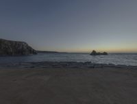 sunset view of rock formations with beach and ocean in background at dusk with blue sky