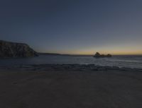 sunset view of rock formations with beach and ocean in background at dusk with blue sky