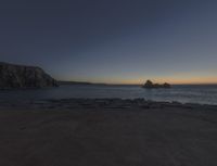 sunset view of rock formations with beach and ocean in background at dusk with blue sky