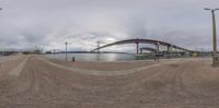 the view of a bridge from a beach looking at the water and boats out in the distance