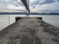 a bridge that crosses the water under a partly cloudy sky during the day with only one person