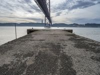 a bridge that crosses the water under a partly cloudy sky during the day with only one person