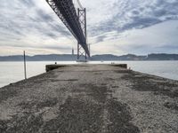 a bridge that crosses the water under a partly cloudy sky during the day with only one person