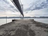 a bridge that crosses the water under a partly cloudy sky during the day with only one person