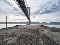 a bridge that crosses the water under a partly cloudy sky during the day with only one person