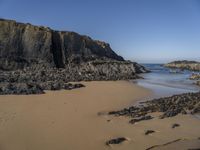 two small surfboards are on the beach near the cliffs that surrounds it with large rocks, and in the water there is sand