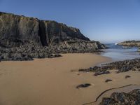 two small surfboards are on the beach near the cliffs that surrounds it with large rocks, and in the water there is sand