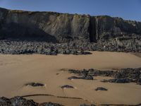 a photo of a person standing on a beach in front of cliffs, looking out