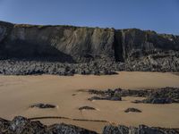 a photo of a person standing on a beach in front of cliffs, looking out