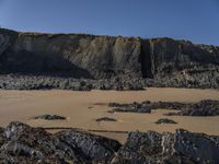 a photo of a person standing on a beach in front of cliffs, looking out