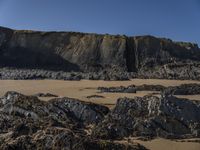 a photo of a person standing on a beach in front of cliffs, looking out