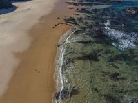 an aerial view of a beach at low tide with large rocks in the distance and blue sky