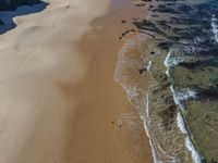 an aerial view of a beach at low tide with large rocks in the distance and blue sky