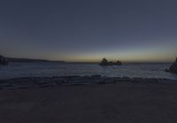 the view of the ocean and its moon at night from a rocky coastline area by the water