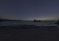 the view of the ocean and its moon at night from a rocky coastline area by the water