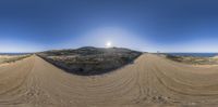 a view of the sun from behind some sand dunes while riding a skate board on dirt track