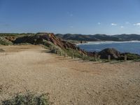 a beach with some rocks and a hill in the background a sign reads one way