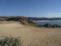 a beach with some rocks and a hill in the background a sign reads one way