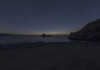 a long exposure photo of rocks along the ocean on a clear night time with the sun rising