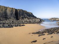 a person is carrying an umbrella along the beach near the water and rocky cliff formations