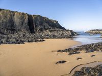 a person is carrying an umbrella along the beach near the water and rocky cliff formations