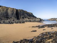 a person is carrying an umbrella along the beach near the water and rocky cliff formations