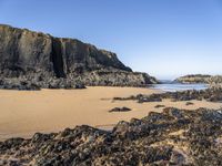 a person is carrying an umbrella along the beach near the water and rocky cliff formations