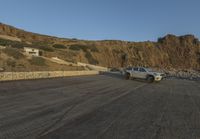 two cars are parked on the road in front of a mountain and ocean shore resort