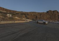 two cars are parked on the road in front of a mountain and ocean shore resort